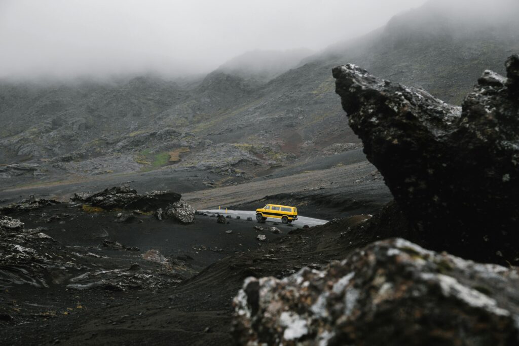A yellow car drives through a misty volcanic landscape, creating a serene and dramatic scene.