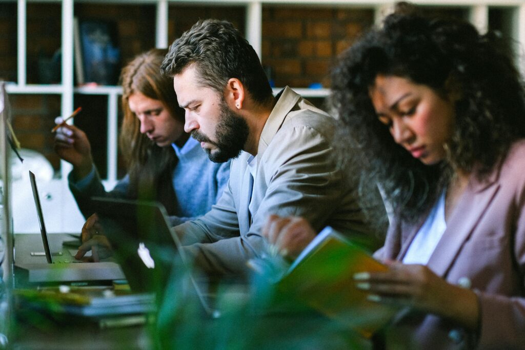 Diverse team focused on their laptops and books in a modern office setting.