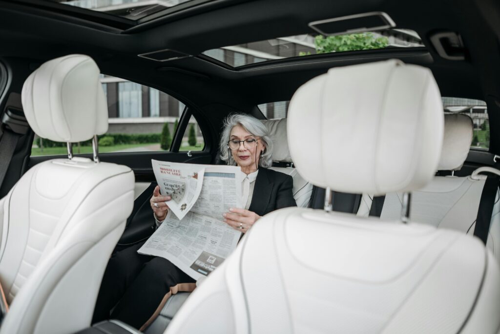 Elderly woman in car reading a newspaper, showcasing a moment of relaxation and focus.