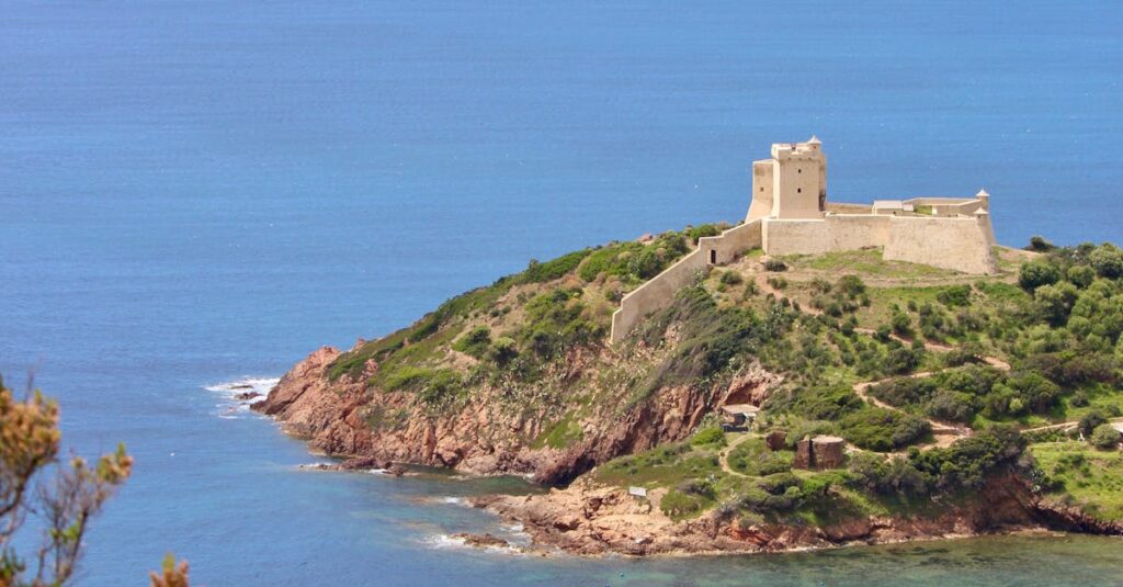 A stunning aerial view of a castle on the Corsican coast with a yacht in the blue sea.